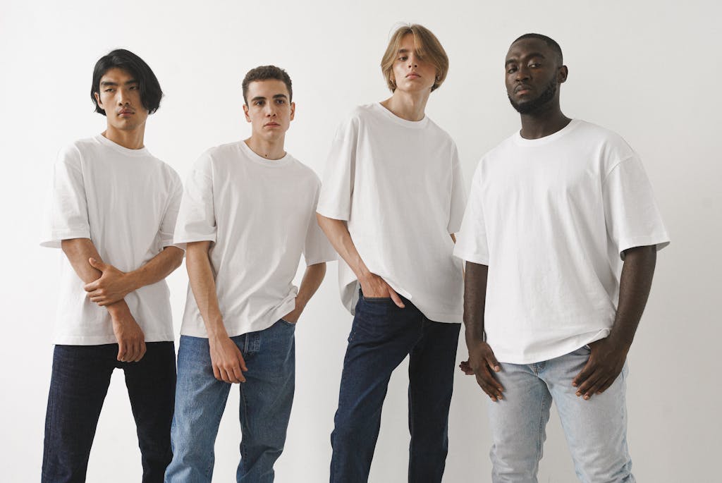 A group of four diverse men modeling white t-shirts and jeans in a studio setting.